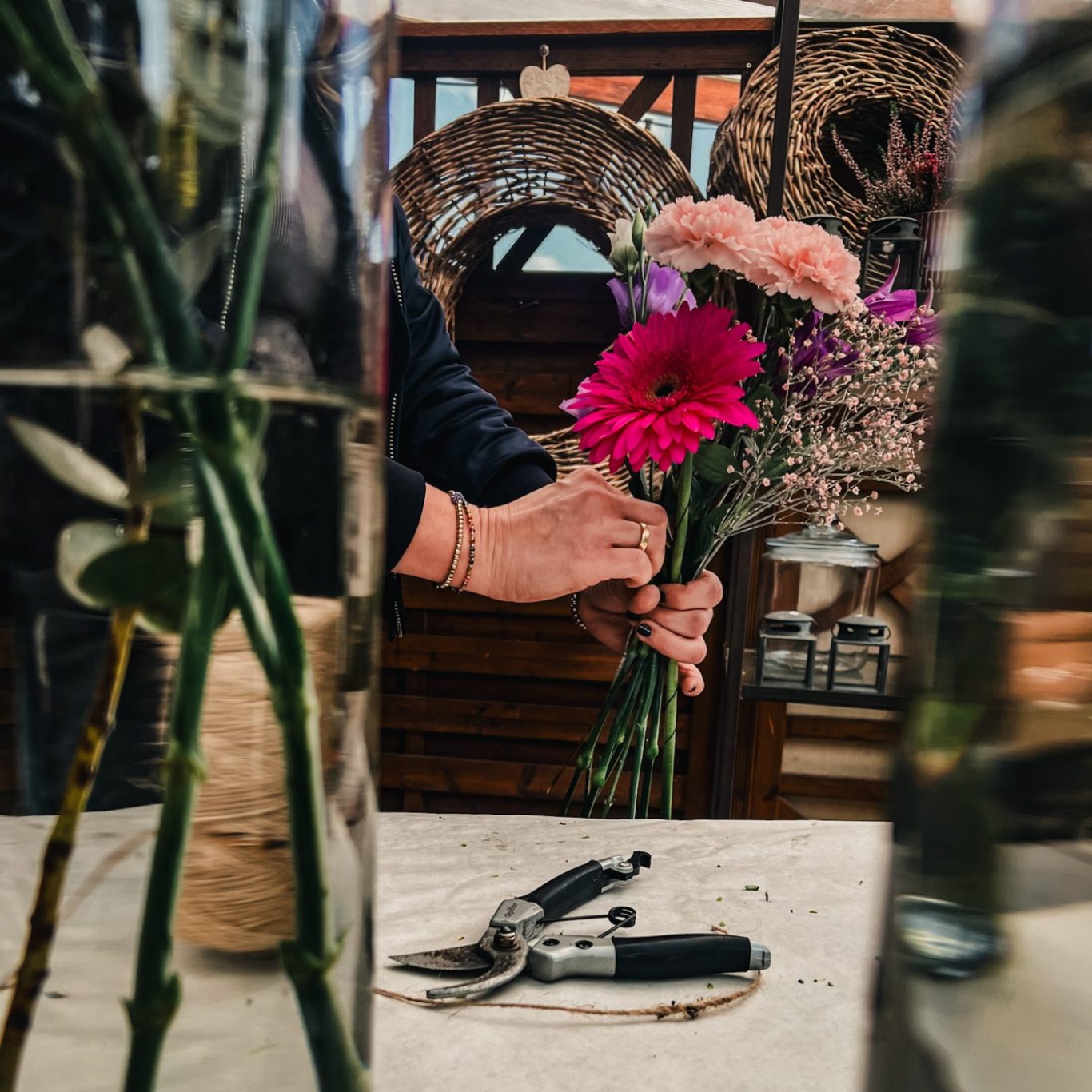 blumenundideen_blumenbinden Eine Hand hält einen Strauß mit bunten Blumen zwischen Vasen und Werkzeug.