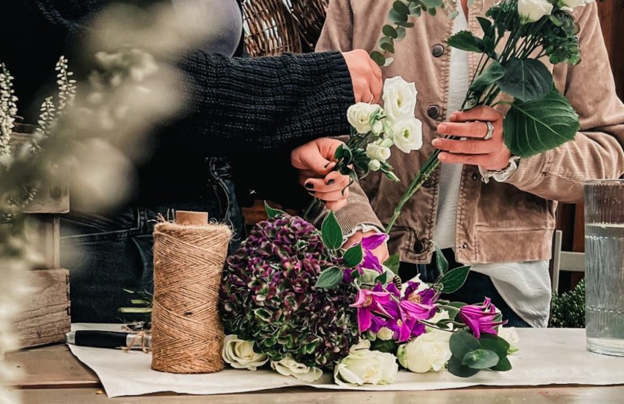 Blumenundideen_workshop Hände binden Blumensträuße mit verschiedenen Blumen und einer mit Schnur umwickelten Rolle.